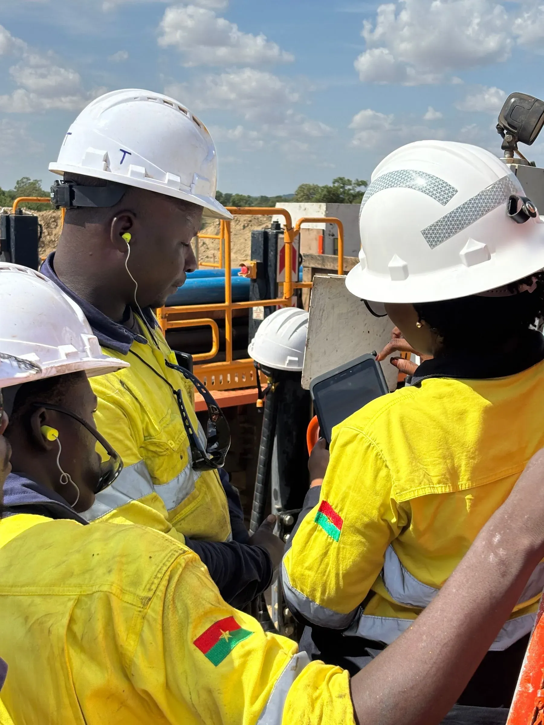 Three drillers in hard hats gather around the tablet at the rig